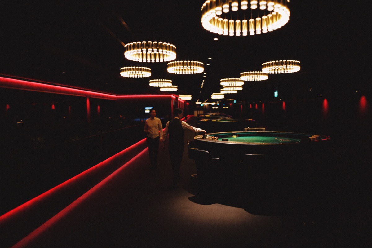 The floor seen from inside the cashier's cage, the counter grille in the foreground and rows of gold lit cabinets and crimson tables beyond it