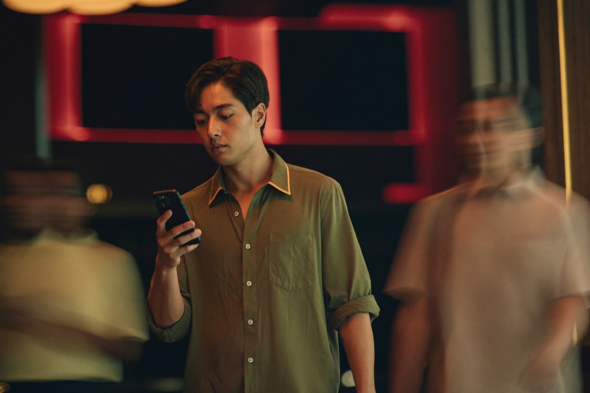 A phone held in both hands on a casino floor with a dark screen catching the gold light, cabinets and a seated player out of focus behind the hands