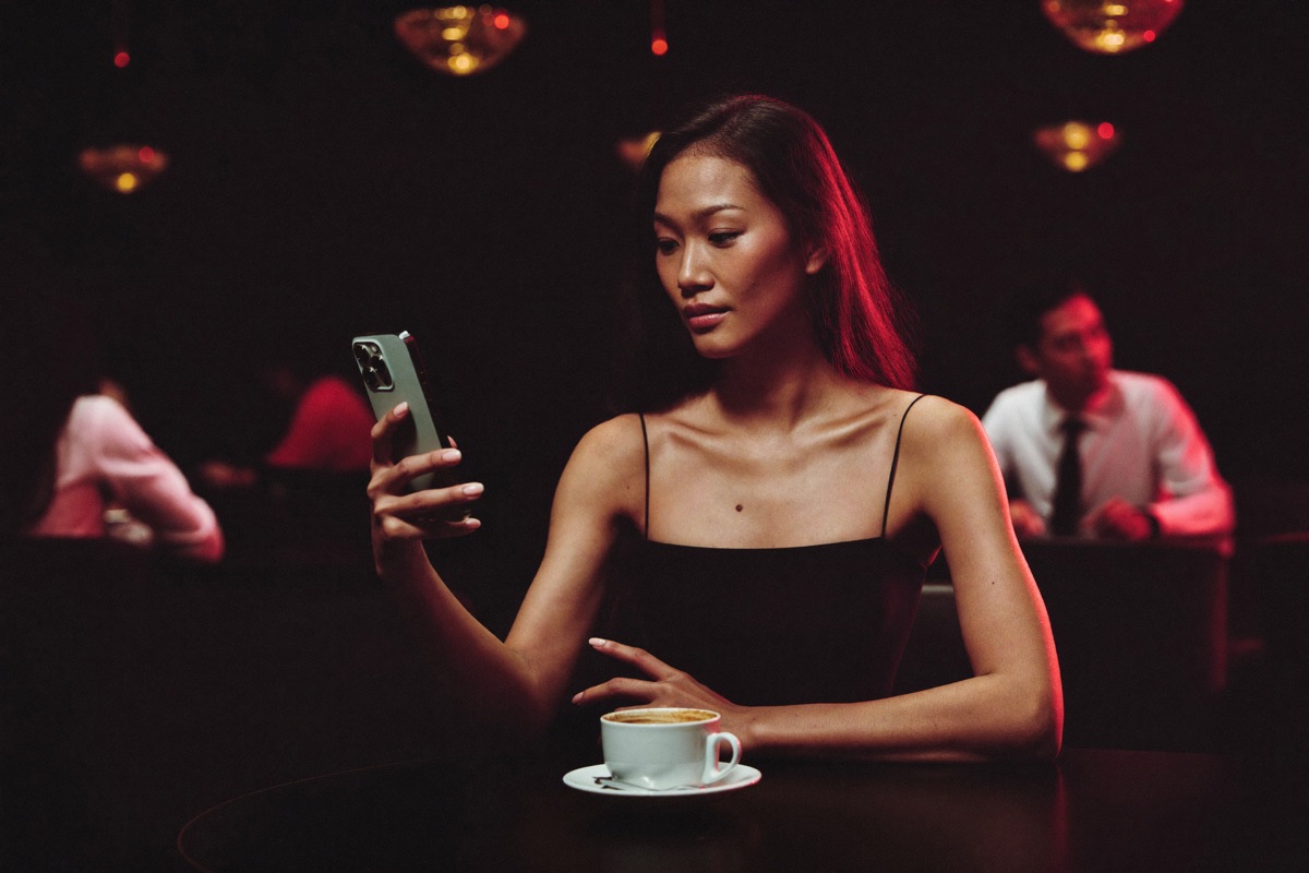 A woman at the entrance arch of a casino floor tapping a passcode into her phone, crimson and gold light spilling out of the room behind her