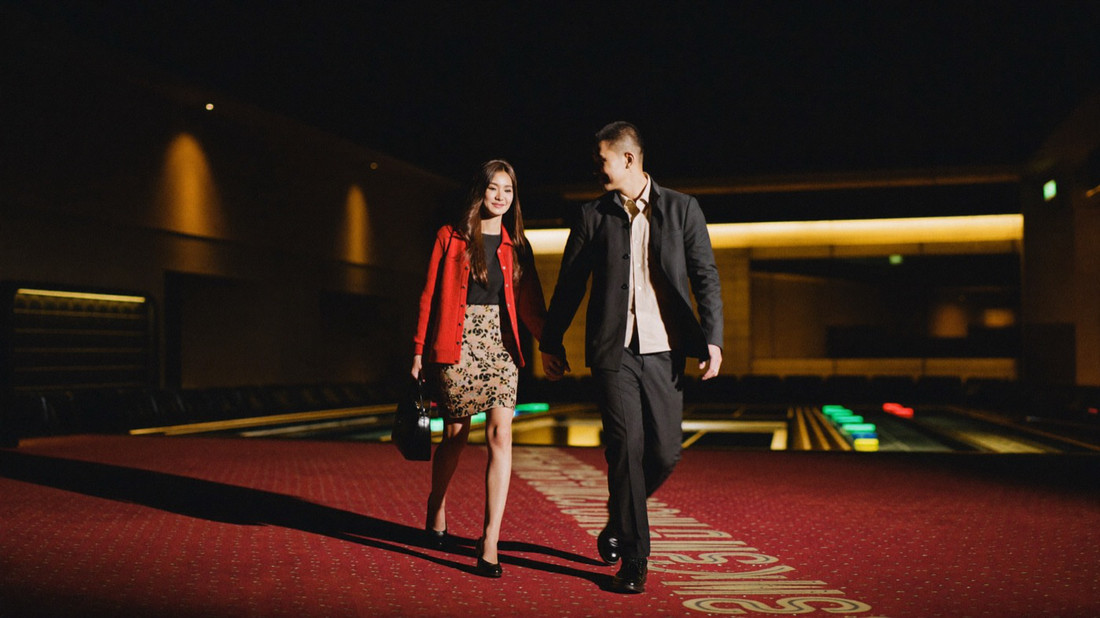A dealer pushing a doubled stack of gold chips across crimson felt toward a seated guest