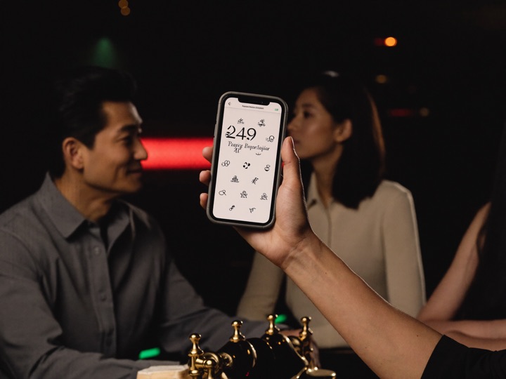 A hand holding up a phone with a dark empty screen in front of a gold lit cabinet, a second phone face down on the ledge beside it