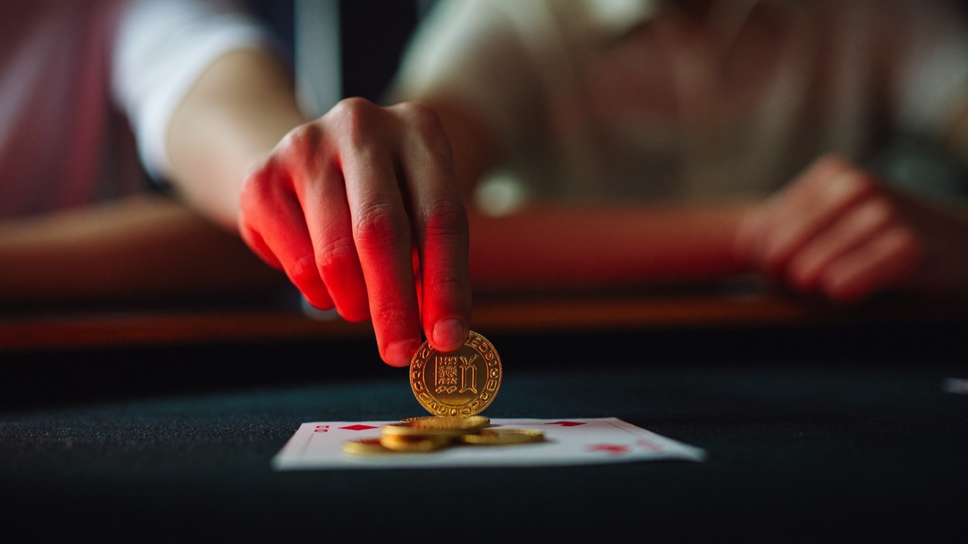 A host in crimson handing one gold chip to a young man at the entrance of the floor